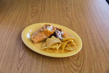 Hawaiian roll with side of chips on yellow plate on wooden table