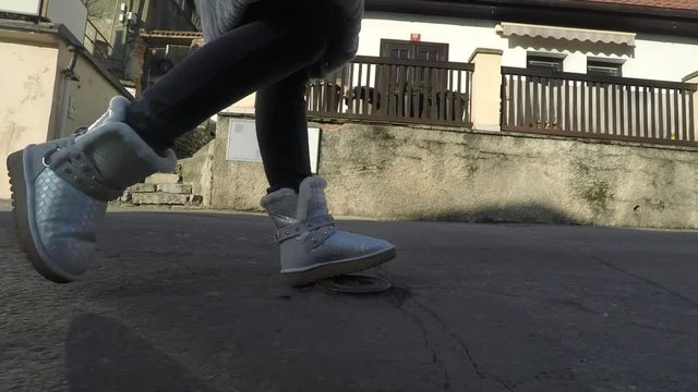 Legs of woman in fur boots walking on bad asphalt