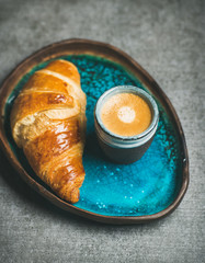 Cup of espresso coffee and croissant in turquoise blue ceramic tray over grey concrete background, selective focus