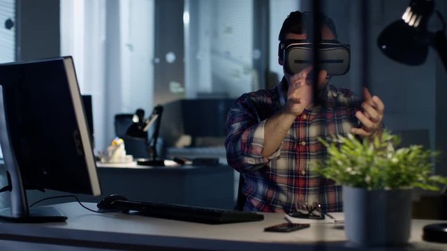Late at Night. Virtual Reality Engineer/ Developer  Wearing VR Headset Creates Content. He's Alone. Office is Illuminated by Moonlight. Shot on RED Cinema Camera 4K (UHD). 