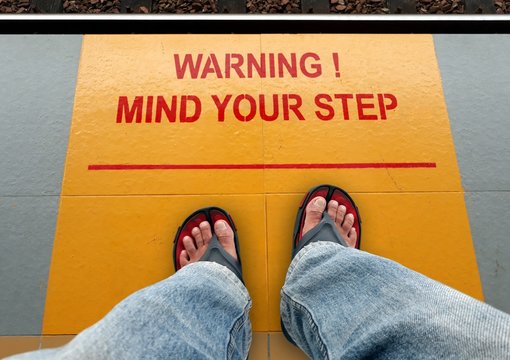 Mind your step signage on a train platform with a man standing