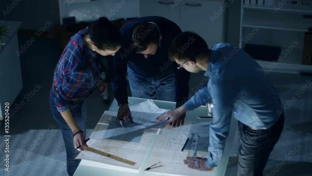 Poster late at night team of design engineers work with drafts and documents on illuminated table. shot on 