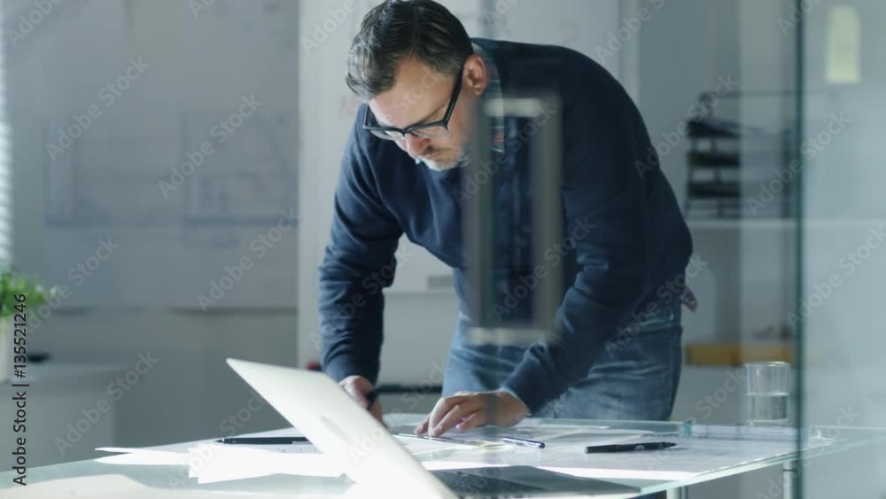Poster late at night design engineer works on documents and drafts at the table. around him on the walls pi