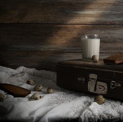 rustic still life with an old suitcase, a glass of milk and eggs on a background of a rough wooden wall