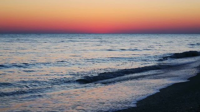 Looping video features a beautiful scene with the setting sun painting the sky above waves breaking gently on a sandy Florida Beach at Lover Key.
