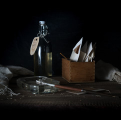 Still Life with a box of letters, bottle and smoking a cigarette. dark background. vintage