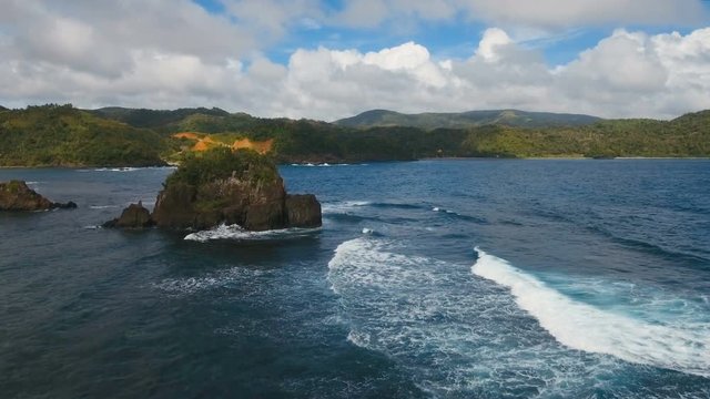 The coast of the tropical island with the mountains and the rainforest on a background of ocean with big waves.Aerial view: sea and the tropical island with rocks and waves. Seascape: sky, clouds