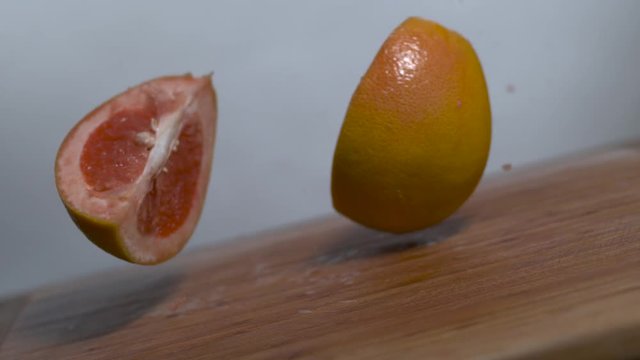 Grapefruit slices falling in slow motion onto a cutting board, rotating shot