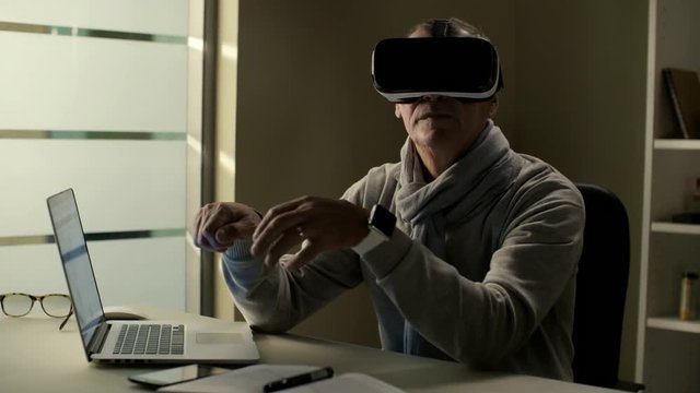 Elderly man in casual clothes wearing a virtual reality headset VR glasses and training to use cyberspace interface