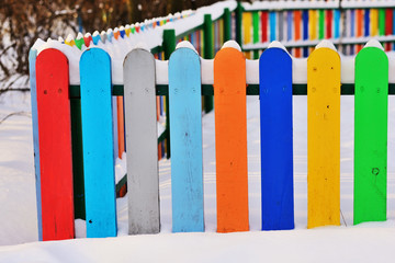 Part of Colourful vertical wooden fence painted in red, blue, green, orange, yellow and gray colors under snonw