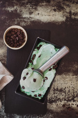 Green tea  ice cream in a metal tray with scoop and dark chocolate chips inside bowl