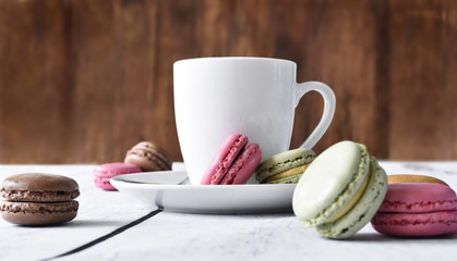 Fototapeta na wymiar Delicious colorful macarons with cream and coffee cup. Coffee break scene with macaron candy and selective focus.