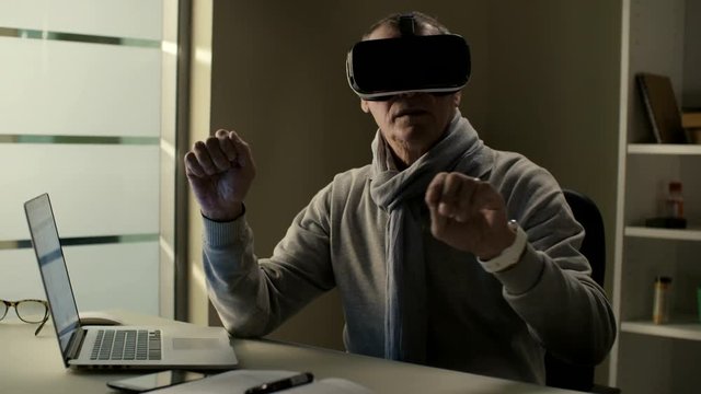 Elderly man in casual clothes wearing a virtual reality headset VR glasses and training to use cyberspace interface