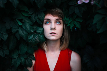 girl with blue eyes peeking out of green bushes