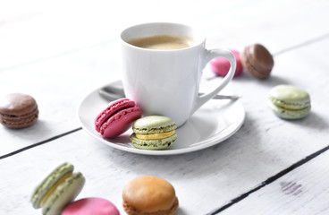 Delicious colorful macarons with cream and coffee cup. Coffee break scene with macaron candy and selective focus.