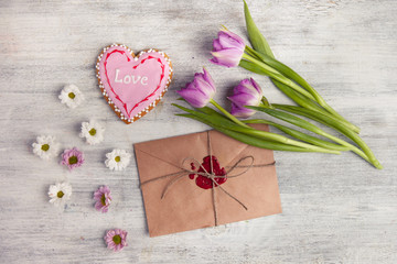 Envelope with wax seal and tulips on wooden background.