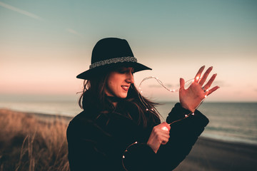 Cuore luminoso tenuto in mano da una ragazza vestita di nera sulla spiaggia al tramonto. San...