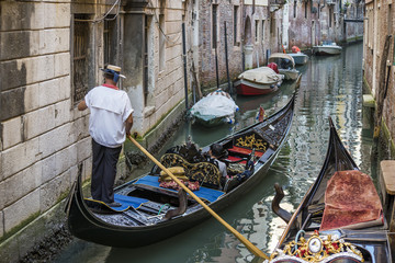 Fototapeta na wymiar Typical gondola with standing gondolier in a narrow canal, Venice, Italy