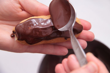 Eclairs or profiterole with chocolate and whipped cream. Spreading chocolate on top of eclair with spoon. Pastry Eclair imposes on a layer of melted chocolate with a spoon.