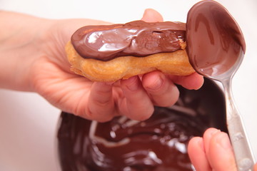 Eclairs or profiterole with chocolate and whipped cream. Spreading chocolate on top of eclair with spoon. Pastry Eclair imposes on a layer of melted chocolate with a spoon.