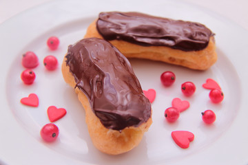 Chocolate eclairs on plate on white background sprinkled with red currant berries and hearts