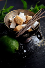 charming still life with lime, mint, bronze bowl with brown and white sugar and vanilla pods
