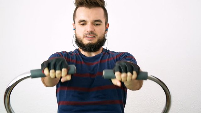 Young bearded man exercising on the rowing machine, isolated on white background.