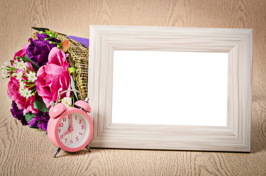 Blank wooden photo frame and pink alarm clock.