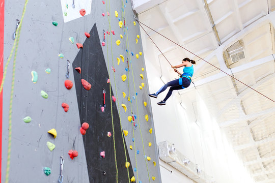 Woman or Girl exercises on indoor rock climber wall hanging on a rope