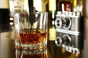 Glass of brandy or cognac and retro camera on the mirror wooden table