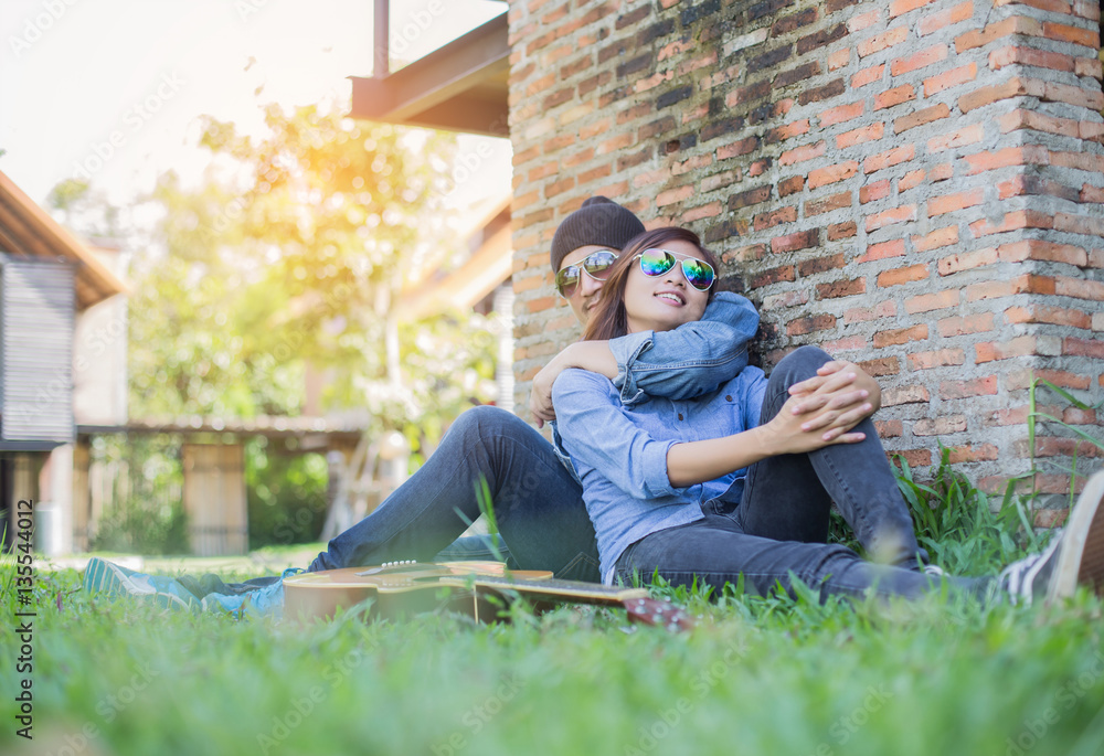 Wall mural Hipster man playing guitar for his girlfriend outdoor against br