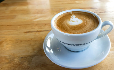 A cup of coffee with latte art in a white cup on wooden table ba