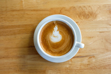 A cup of coffee with latte art in a white cup on wooden table ba