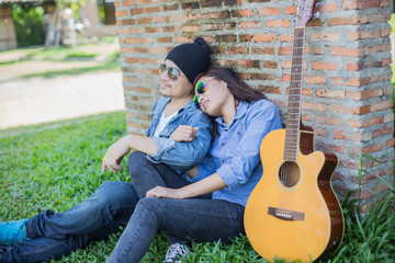 Hipster man playing guitar for his girlfriend outdoor against br
