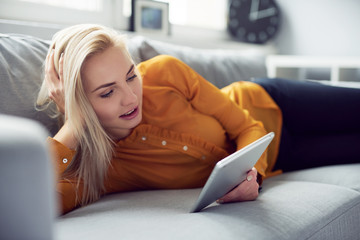 Young woman browsing internet on her tablet lying on the sofa at home