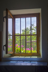 Open window with metal bars, bright summer day outdoors - darkness indoors