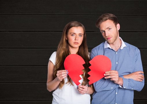 Portrait of sad couple holding broken hearts