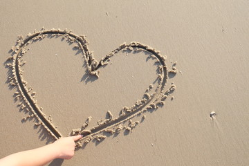 woman drawing a heart in the sand on beach, sunset time. Valentine's concept.