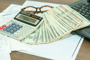 Obraz premium Finance concept : The United States hundred-dollar bills , calculator , bills ,eyeglasses and laptop on the table 