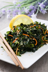 Wakame salad with carrot, sesame seeds and lemon juice in plate on wooden table
