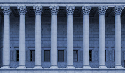 Corinthian columns in a colonnade of a building facade. The neoclassical style resembles a law court / courthouse, university, library or public administration building. Blue color tone. - obrazy, fototapety, plakaty