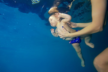Fototapeta na wymiar Mom coach teaches baby to swim underwater in the pool and maintains his hands. Portrait. Shooting under water. Bottom view. Landscape orientation