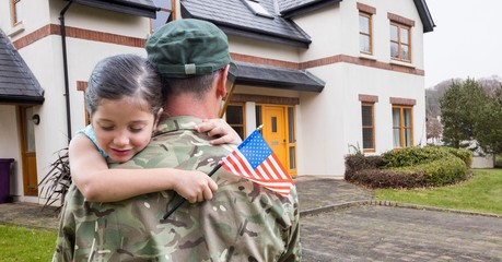 American soldier carrying girl in front of a house