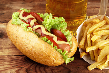 Hot dog with glass of beer with french fries on wooden board