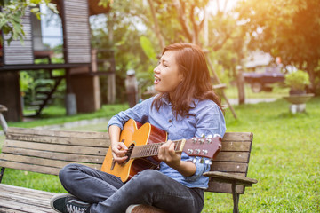Beautiful young woman playing guitar sitting on bench, Happy tim