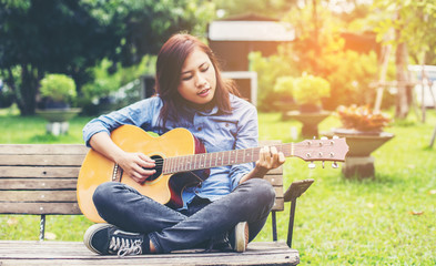Beautiful young woman playing guitar sitting on bench, Happy tim