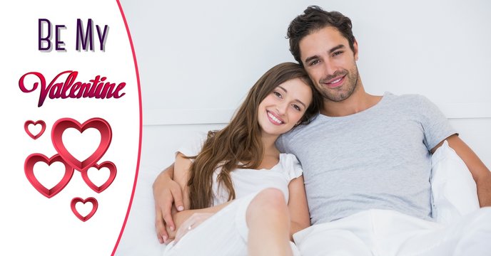 Smiling couple in bed with red heart shapes and valentine text