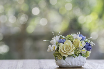 Artificial flowers in a vase on wood and background bokeh.