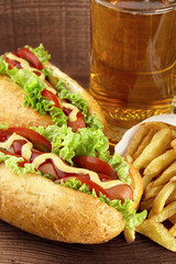 Hot dogs with glass of beer with french fries on wooden board