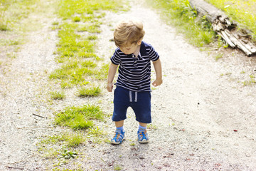 A little boy walks outdoors. The kid walks on the green grass.

